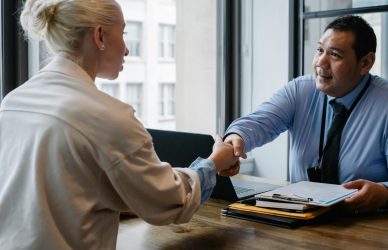 Two professionals in an office setting shaking hands after a business agreement.